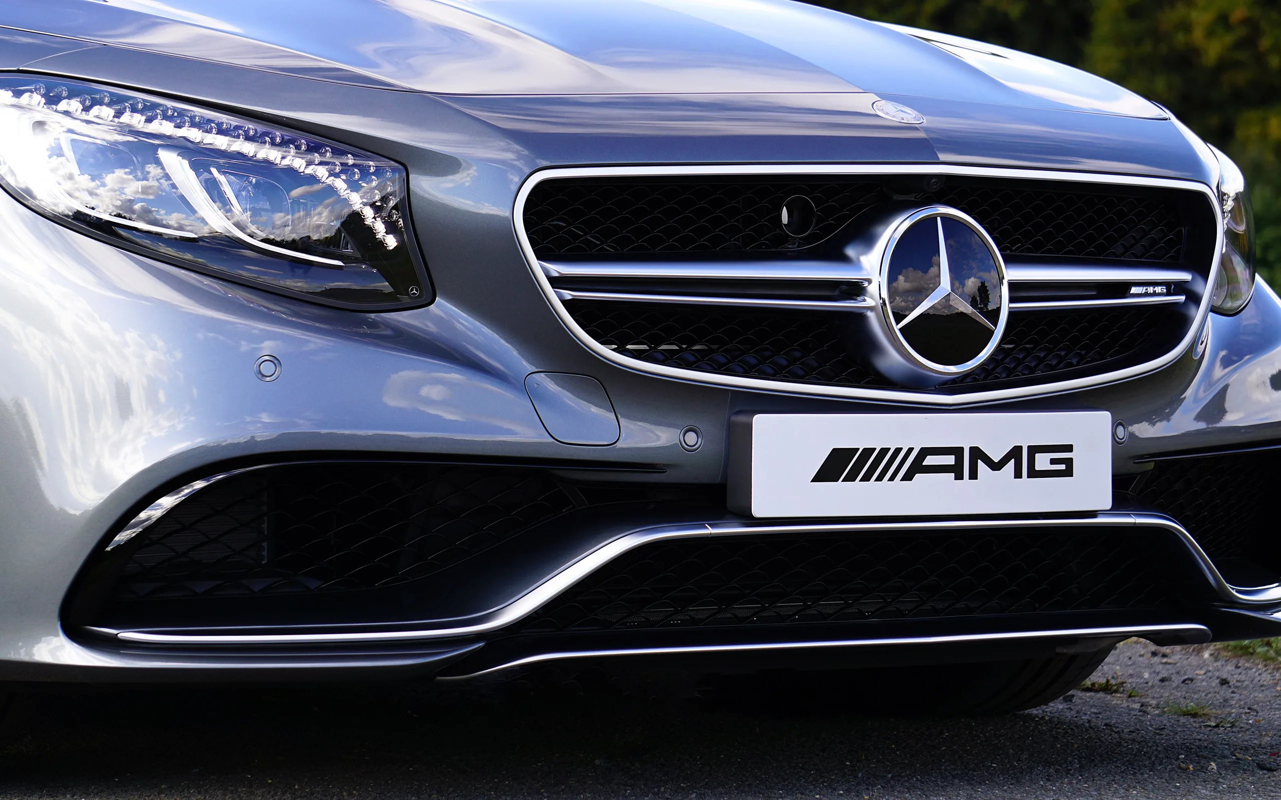 Façade d’une calandre de voiture avec emblème central : logo circulaire monté sur la grille et reflets de carrosserie au sol.